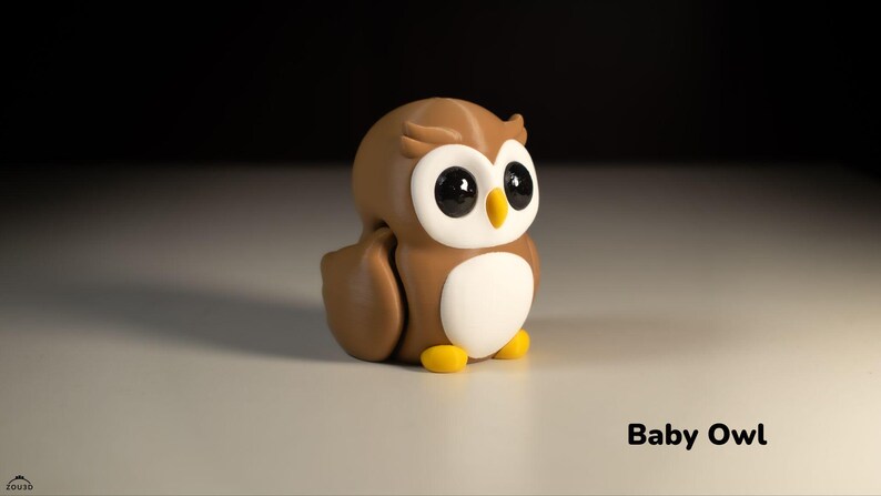 May include: A brown and white owl figurine with large black eyes. The owl is sitting on a white surface. Baby Owl.