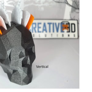 Puede incluir: Un cr&aacute;neo geom&eacute;trico negro y gris con acentos naranja y blanco. El cr&aacute;neo est&aacute; hecho de un material texturizado y tiene una orientaci&oacute;n vertical. El texto "CREATIVE 3D SOLUTIONS" es visible en el fondo.