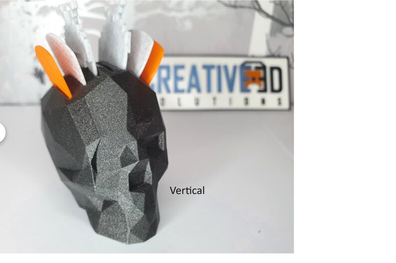 Puede incluir: Un cr&aacute;neo geom&eacute;trico negro y gris con acentos naranja y blanco. El cr&aacute;neo est&aacute; hecho de un material texturizado y tiene una orientaci&oacute;n vertical. El texto "CREATIVE 3D SOLUTIONS" es visible en el fondo.