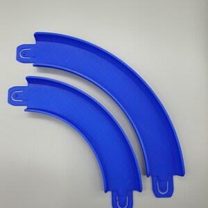 May include: Two blue plastic track pieces for a toy race car track. The pieces are curved and connect together to form a track.