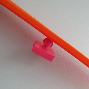 May include: A pink plastic track piece for a toy racing car track. The track piece is attached to a bright orange track piece.