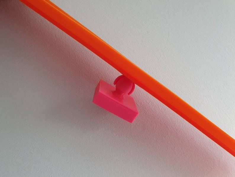 May include: A pink plastic track piece for a toy racing car track. The track piece is attached to a bright orange track piece.