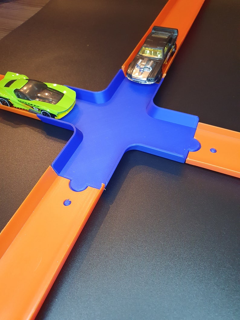 May include: A blue and orange plastic toy race track with two toy cars. One car is green and the other is black.