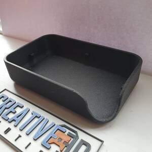 May include: A black plastic tray with a curved edge. The tray is empty and appears to be made with a 3D printer.