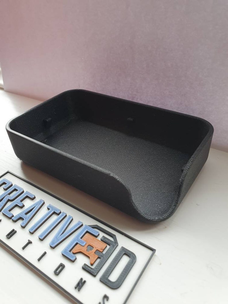 May include: A black plastic tray with a curved edge. The tray is empty and appears to be made with a 3D printer.
