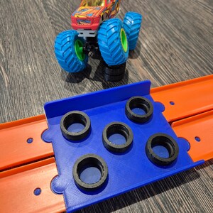 May include: A blue plastic track set with a red, yellow, and black monster truck on top. The track has five black tire-shaped holes.