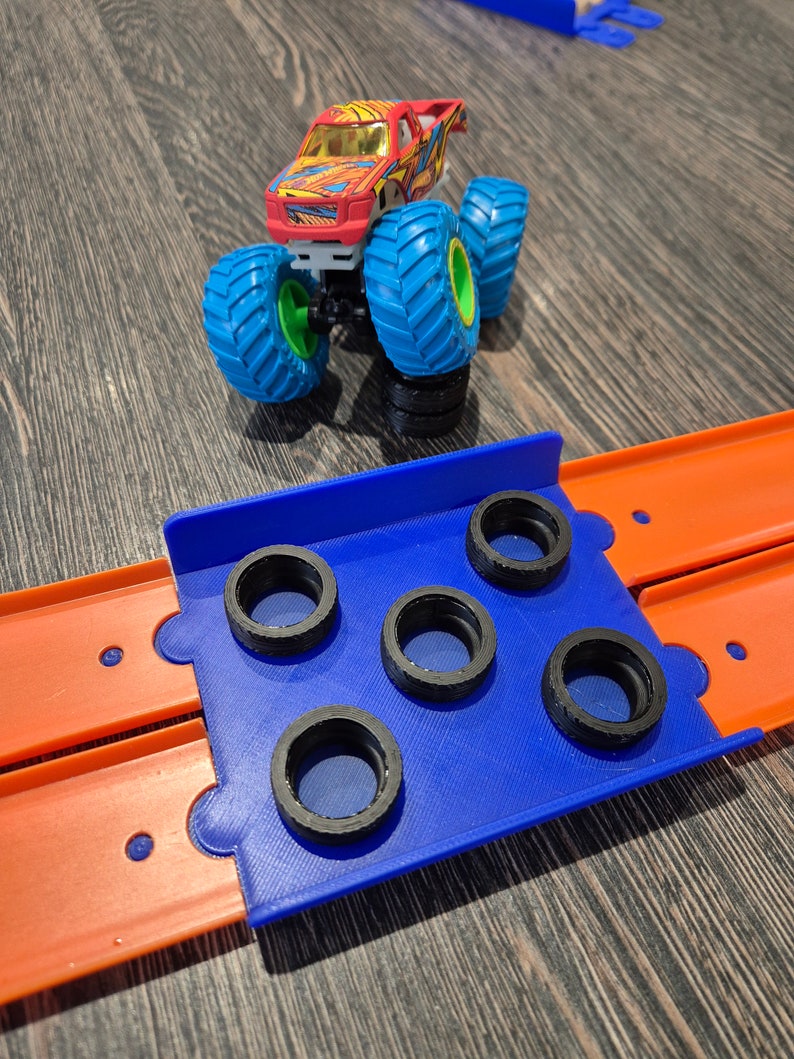 May include: A blue plastic track set with a red, yellow, and black monster truck on top. The track has five black tire-shaped holes.