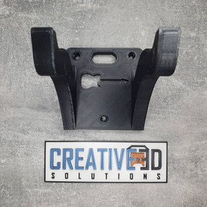 May include: Black 3D printed wall mount for a guitar. The mount has a cutout in the shape of a guitar. The text "CREATIVE3D SOLUTIONS" is printed on a white sticker below the mount.
