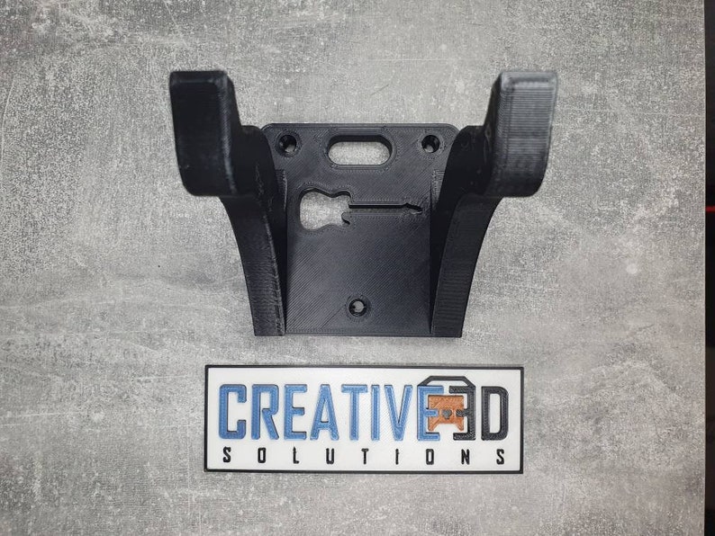 May include: Black 3D printed wall mount for a guitar. The mount has a cutout in the shape of a guitar. The text "CREATIVE3D SOLUTIONS" is printed on a white sticker below the mount.