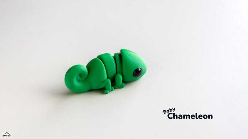 Op de afbeelding: Een groen, gesegmenteerd, plastic kameleon speelgoed met zwarte ogen. Het speelgoed ligt op een wit oppervlak. De tekst "Baby Chameleon" is onder het speelgoed gedrukt.