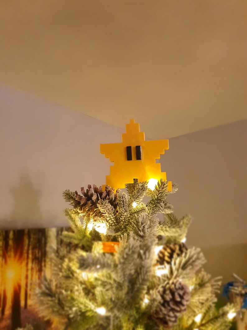Puede incluir: Un adorno de &aacute;rbol de Navidad en forma de estrella amarilla con ojos negros, que se asemeja a un personaje de videojuego.
