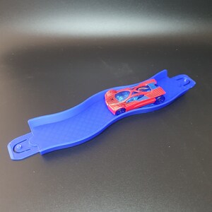 May include: A blue plastic track with a red toy car with a spider web design on it.