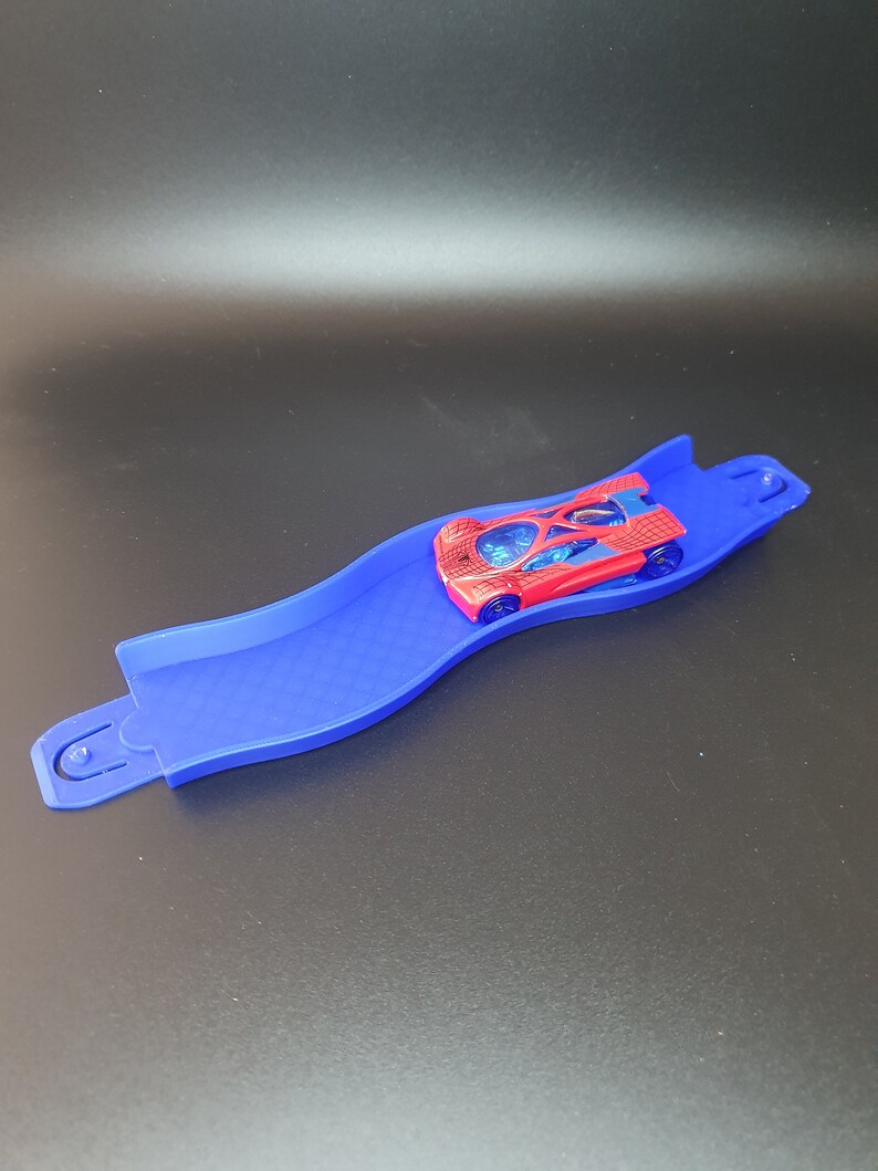 May include: A blue plastic track with a red toy car with a spider web design on it.