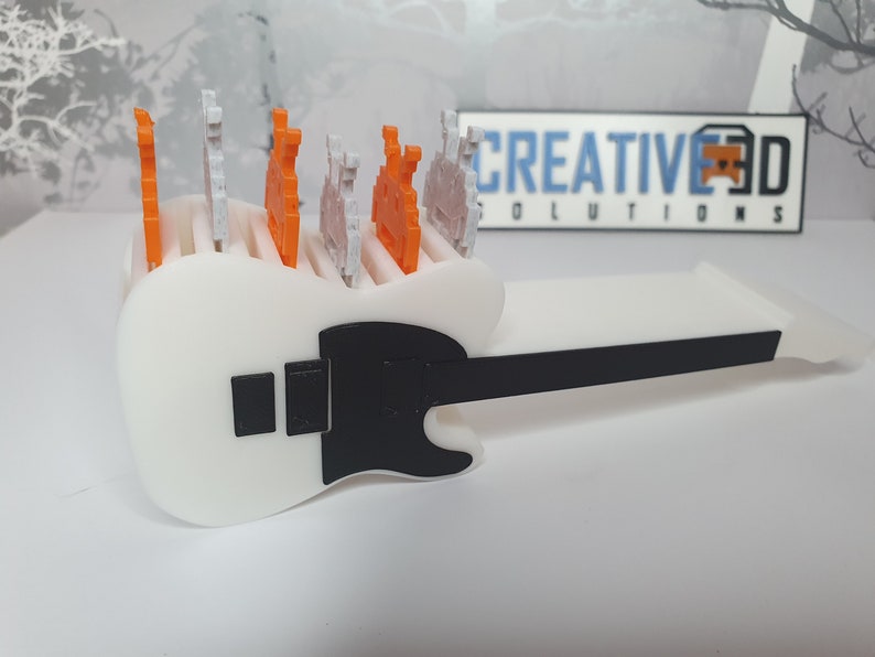 May include: A white guitar-shaped holder with a black pickguard and a black neck. The holder has slots for small figurines, and there are several orange and white figurines in the slots.