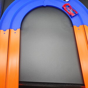 May include: A blue and orange toy race track set with two toy cars, one white and one red, on the track.