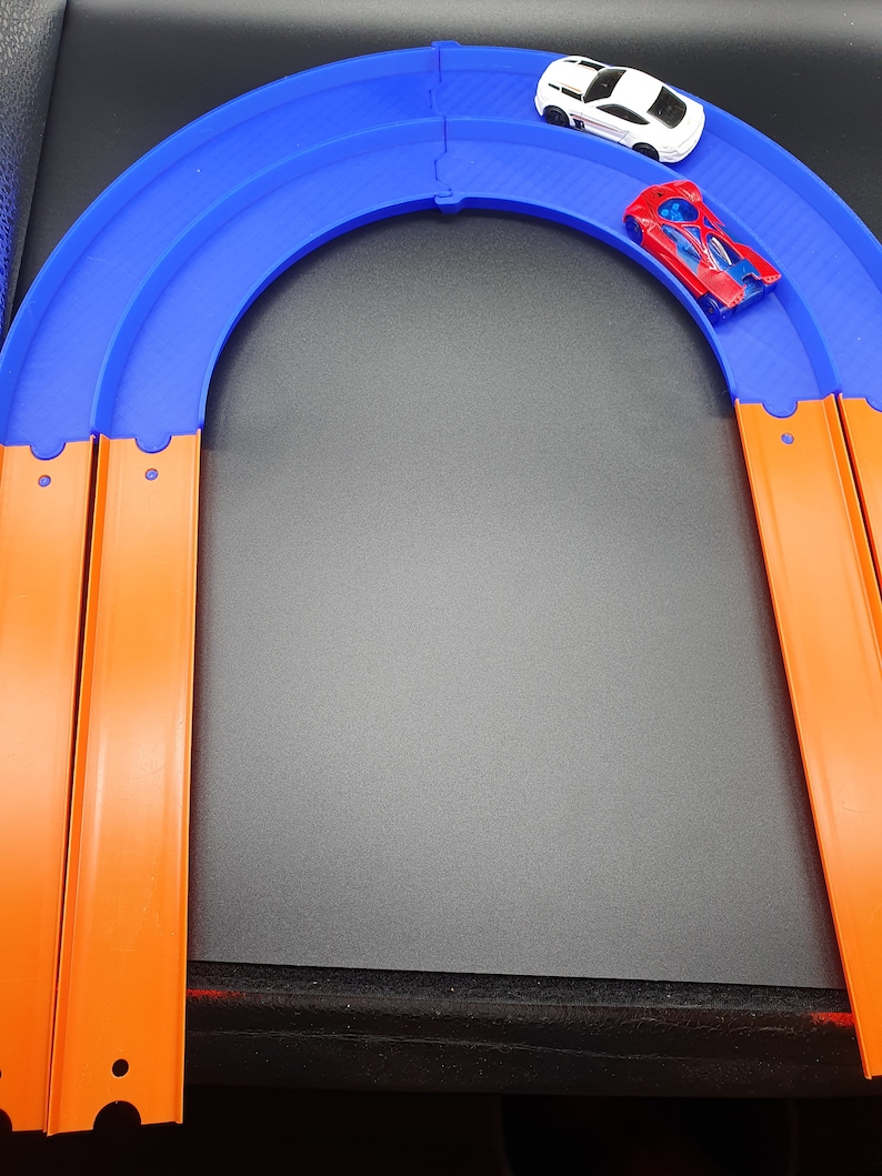 May include: A blue and orange toy race track set with two toy cars, one white and one red, on the track.