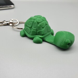 May include: A green plastic turtle keychain with a silver metal ring. The turtle has a detailed shell and a long neck.