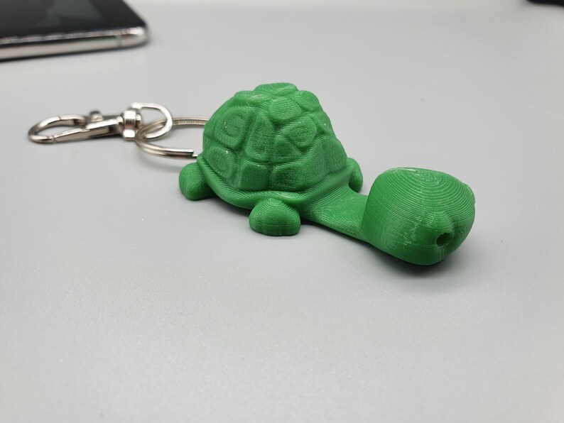May include: A green plastic turtle keychain with a silver metal ring. The turtle has a detailed shell and a long neck.