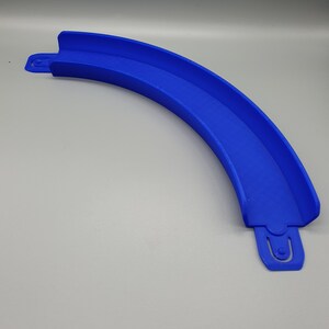 May include: A blue plastic track piece for a toy racing car track. The piece is curved and has a groove for the car to run in.