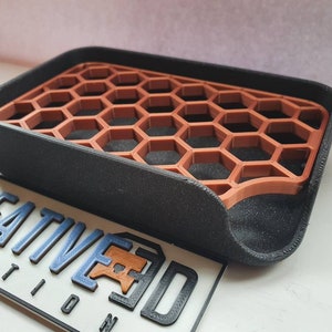 May include: A black soap dish with a honeycomb-shaped insert made of brown plastic. The dish has a curved edge and is designed to drain water.