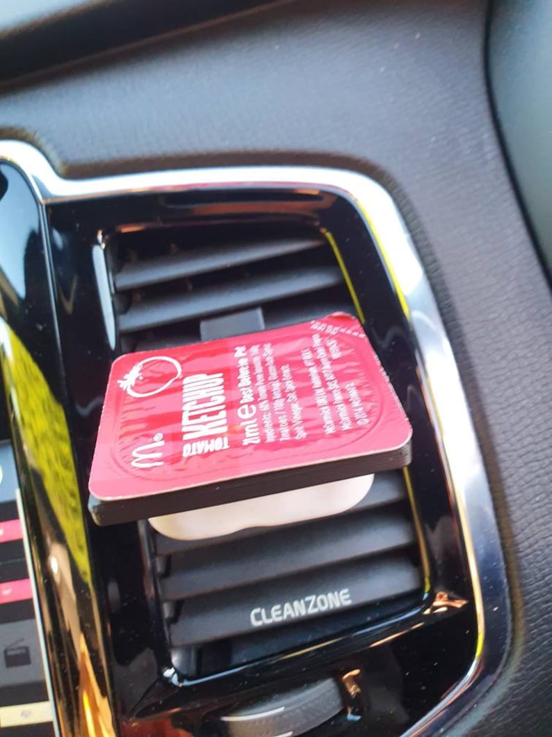 Pu&ograve; includere: Un deodorante per auto rosso con la scritta "Mr. & Mrs. Tomato" e "Fresh Up". Il deodorante &egrave; attaccato alla bocchetta di aerazione di un'auto.