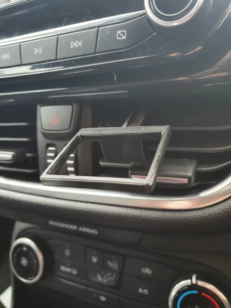 May include: A black plastic phone holder designed to fit into a car's air vent.