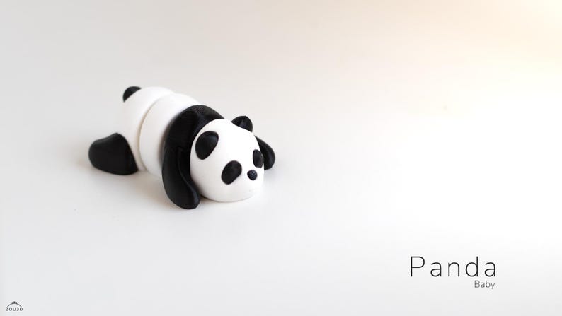 May include: A small, stylized panda figurine in black and white, lying down on a white surface. The panda has black ears, eyes, and limbs, with a white body. The word "Panda" and "Baby" are written in a minimalist font.