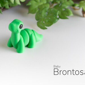 May include: A small, green, plastic dinosaur toy shaped like a baby Brontosaurus. The toy has black eyes and a friendly expression.