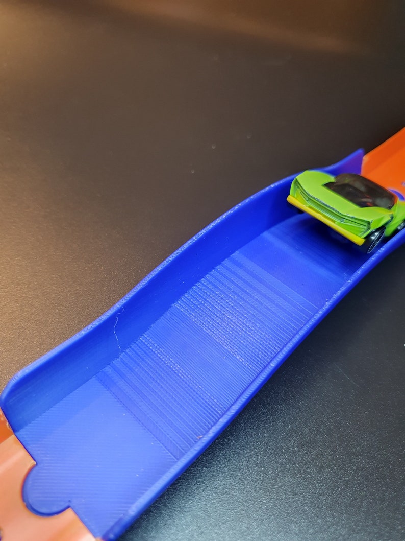 Op de afbeelding: Een blauwe en oranje plastic speelgoed racebaan met een groene speelgoedauto op de baan.