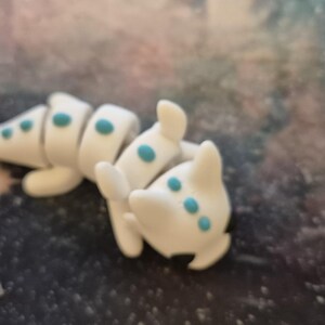DragonWhirl™ Baby Dragon Fidget Keyring: "A small, detailed baby dragon keyring in vibrant, hand-painted colors. The dragon is depicted sitting with tiny wings, a curled tail, and playful, wide eyes. Its smooth texture and intricate scales
