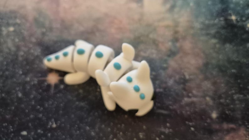 DragonWhirl™ Baby Dragon Fidget Keyring: "A small, detailed baby dragon keyring in vibrant, hand-painted colors. The dragon is depicted sitting with tiny wings, a curled tail, and playful, wide eyes. Its smooth texture and intricate scales