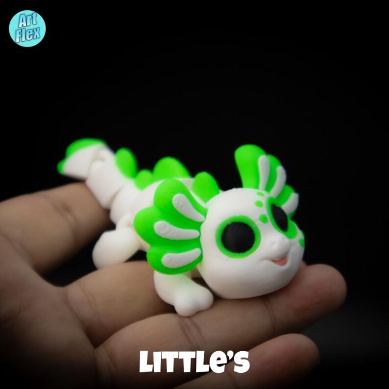 May include: A white and green axolotl figurine with black eyes. The figurine is sitting on a hand.