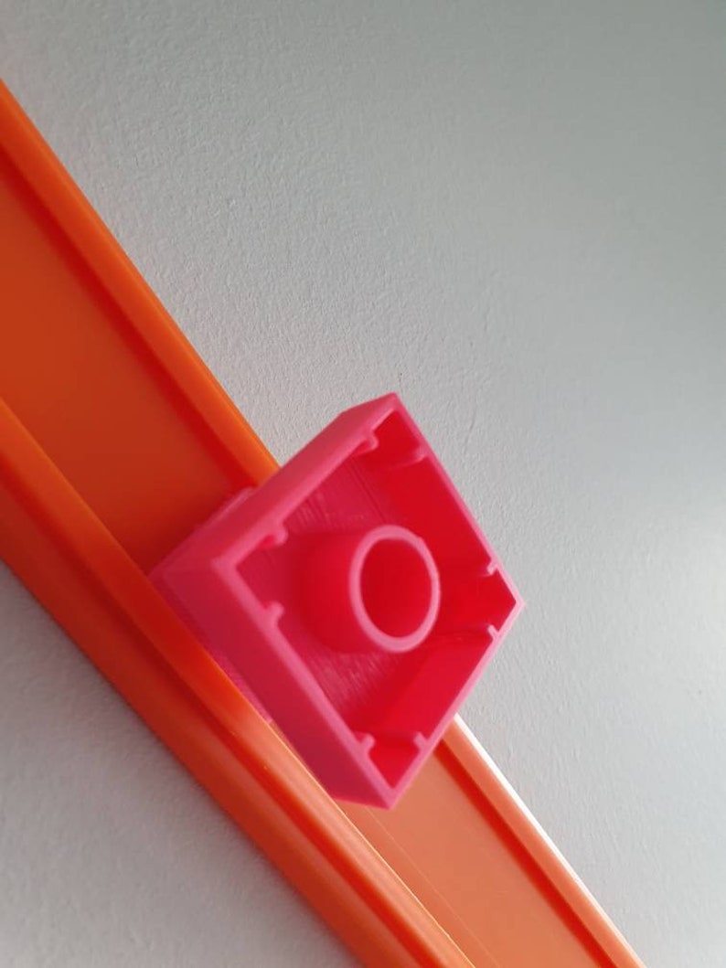 May include: A pink plastic track piece with a round hole in the centre. The track piece is designed to connect to other track pieces to create a race track.