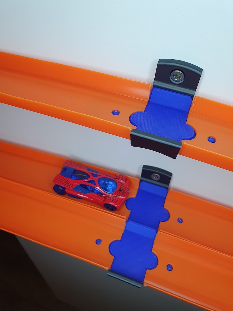 May include: Two orange Hot Wheels track pieces with blue and black plastic connectors. A red toy car with a spider web design is on the track.