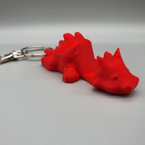 May include: A red 3D printed dragon keyring. The dragon is curled up and has a silver key ring attached.