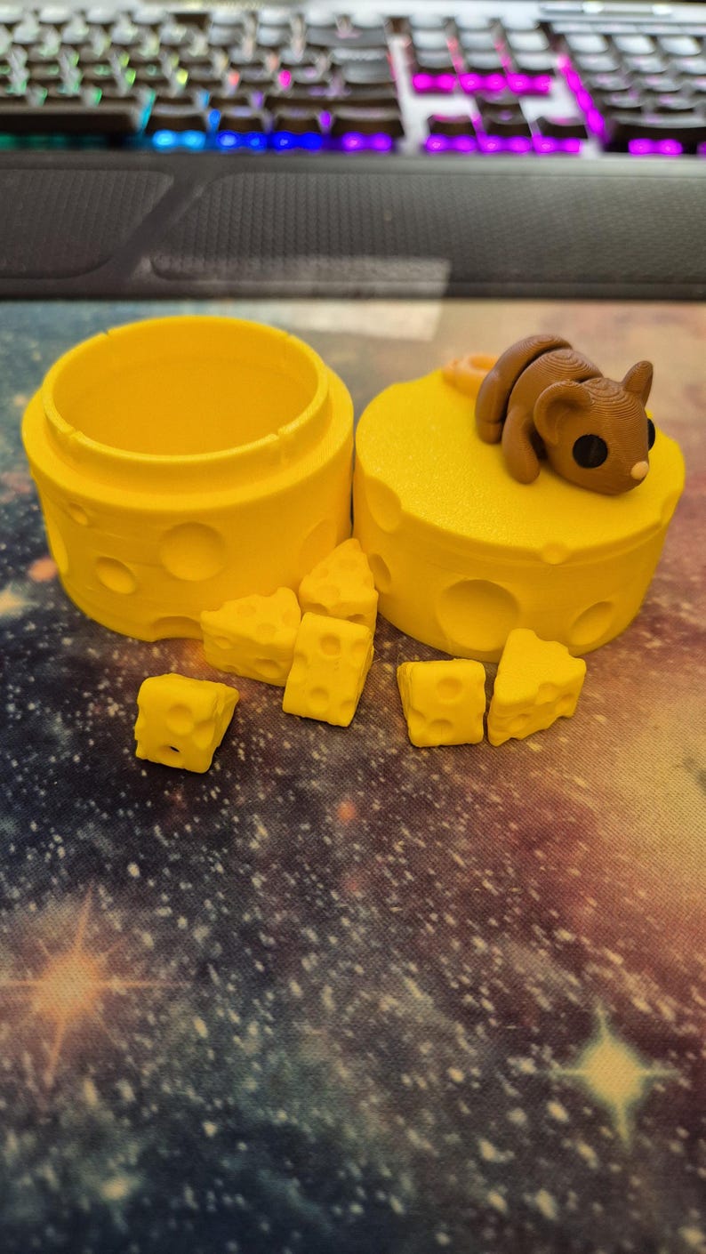 Puede incluir: Un recipiente amarillo con forma de queso con una figurita de rat&oacute;n en la parte superior. El recipiente est&aacute; abierto y hay varias piezas peque&ntilde;as de queso esparcidas a su alrededor.