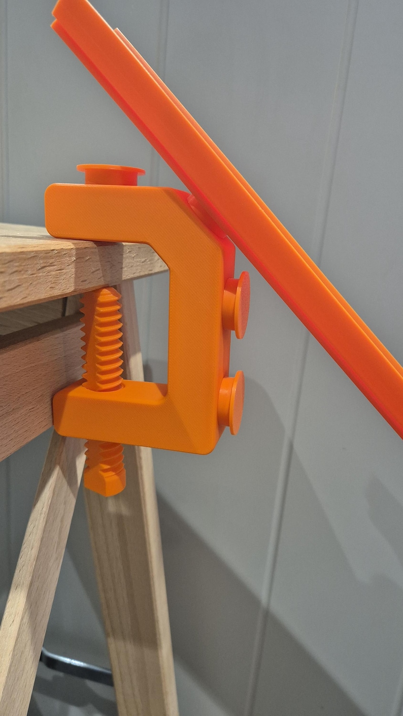 May include: Orange plastic clamp with a screw and two rubber feet. The clamp is attached to a wooden table.