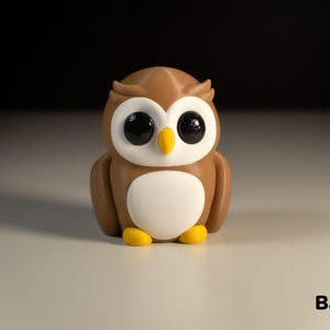 May include: A brown and white owl figurine with large black eyes. The owl is sitting on a white surface. The text "Baby Owl" is written below the owl.