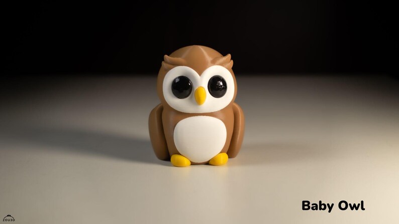 May include: A brown and white owl figurine with large black eyes. The owl is sitting on a white surface. The text "Baby Owl" is written below the owl.