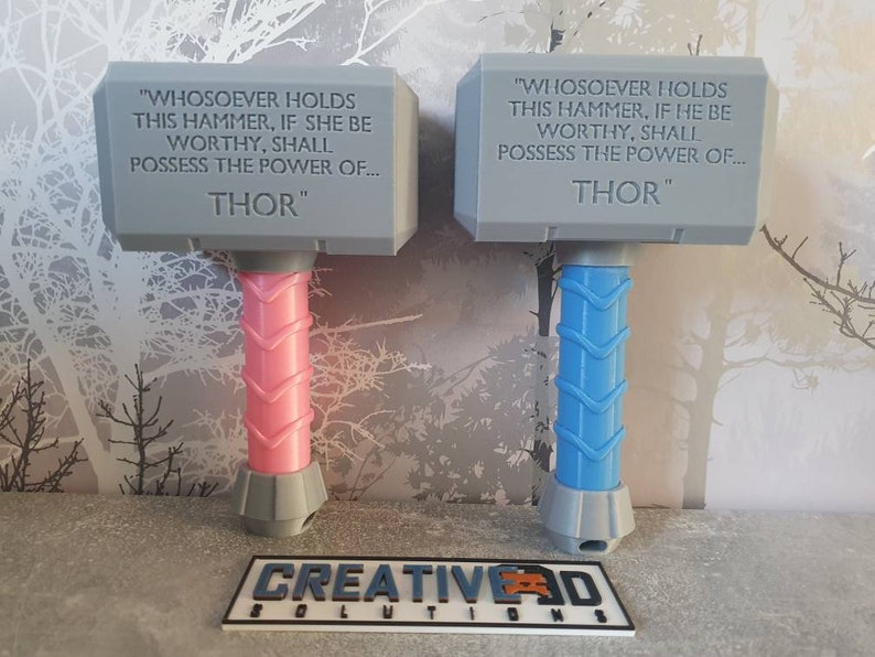 May include: Two gray plastic toy hammers with the inscription "WHOSOEVER HOLDS THIS HAMMER, IF SHE BE WORTHY, SHALL POSSESS THE POWER OF... THOR" and "WIHOSOEVER HOLDS THIS HAMMER, IF HE BE WORTHY, SHALL POSSESS THE POWER OF... THOR". One hammer has a pink handle and the other has a blue handle.