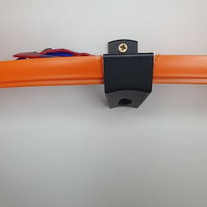 May include: Black plastic wall mount with a screw for hanging a toy race track. The track is orange and has a small red toy car on it.