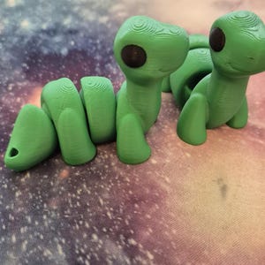 May include: Two green 3D printed worm figurines with black eyes. The worm on the left is curled up and the worm on the right is standing upright.