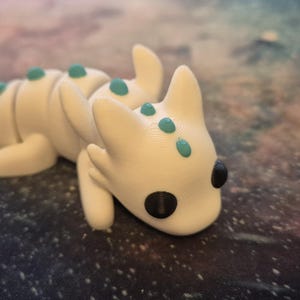 May include: A white dragon figurine with teal accents. The dragon is lying on its belly with its head turned to the side. It has black eyes and a small mouth.