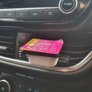 May include: A pink and white condiment container with the text "Honey Mustard" on the lid, sitting in a car's air vent.