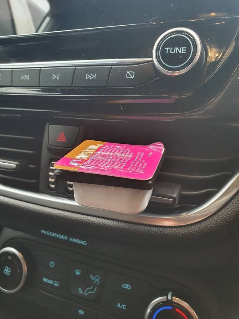 May include: A pink and white condiment container with the text "Honey Mustard" on the lid, sitting in a car's air vent.