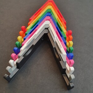 Puede incluir: Un conjunto de diez soportes para tel&eacute;fono de varios colores, incluyendo rojo, naranja, amarillo, verde, azul, morado, rosa, blanco, gris y negro. Los soportes est&aacute;n doblados en forma de V y apilados uno encima del otro.