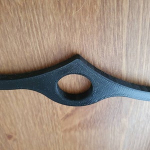 May include: A black plastic bookmark with a curved design and a round hole in the center.