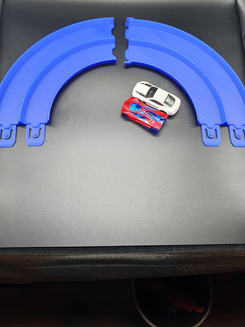 May include: Two toy cars, one red and one white, on a blue plastic race track.