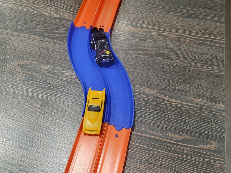 May include: Two toy cars race on a blue and orange track. The yellow car is in the lead, while the black and white police car is behind it.