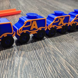 May include: A toy train made of blue and orange plastic with wheels. The train cars are connected and each car has a letter on it, spelling out the word "JAXON".